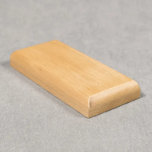 Zdjęcie przedstawiające prostokątną drewnianą podstawkę w kolorze jasnego brązu i frezie zaokrąglonym. Podstawka ma wysokość dwóch centymetrów. Zwrócona do obiektywu w taki sposób, że widać jej front i bok.