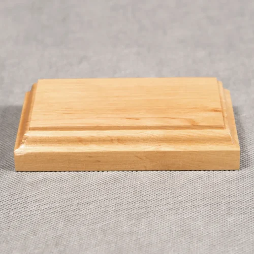 Zdjęcie przedstawiające prostokątną drewnianą podstawkę w kolorze jasnego brązu i frezie klasycznym. Podstawka ma wysokość dwóch centymetrów. Zwrócona jest frontem do obiektywu.