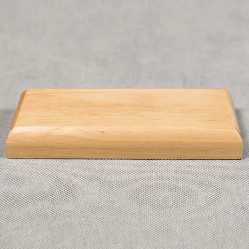 Zdjęcie przedstawiające prostokątną drewnianą podstawkę w kolorze jasnego brązu i zaokrąglonym frezie. Podstawka ma wysokość dwóch centymetrów. Zwrócona jest frontem do obiektywu.