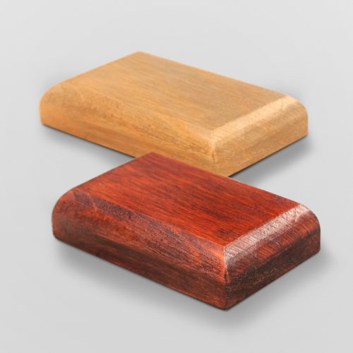 Zdjęcie dwóch podstawek drewnianych o zaokrąglonym frezie ustawionych równolegle względem siebie. Podstawki mają wysokość dwóch centymetrów. Podstawka od tyłu jest jasnobrązowa, a podstawka od frontu ciemnobrązowa.