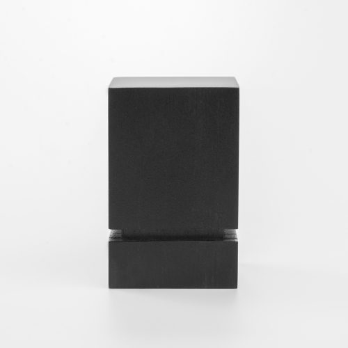 Zdjęcie przedstawiające prostą podstawkę drewnianą polakierowaną na czarno. Skierowana jest frontem do obiektywu. Podstawka ma kształt kolumny o wysokości czterech centymetrów z wycięciem wokół przy podstawie.
