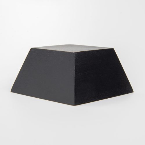 Zdjęcie przedstawiające podstawkę drewnianą polakierowaną na czarno. Podstawka ma kształt piramidki o wysokości czterech centymetrów. Swoim frontem obrócona jest od obiektywu o około 45 stopni.