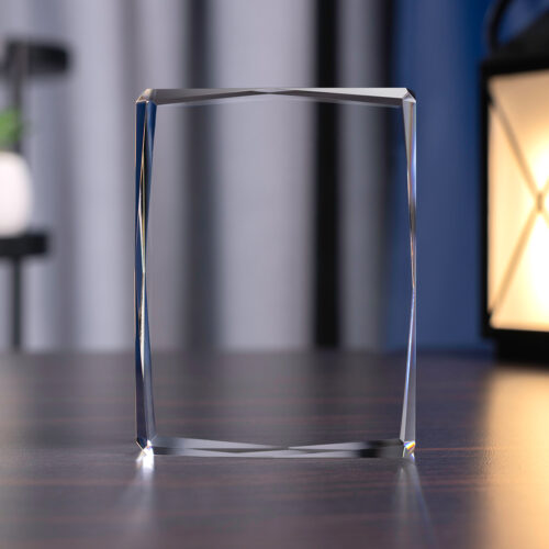 Szklana prostopadłościenna statuetka ze ściętymi krawędziami i wymiarach 12x9x3 cm ustawiona pionowo - widok od frontu. Wykorzystywana jest do tworzenia statuetek firmowych. Możliwe jest grawerowanie w ich trójwymiarowych wzorów. Laser 3D może odzwierciedlić w nich wizerunki budynków, pojazdów, roślin i ludzi.